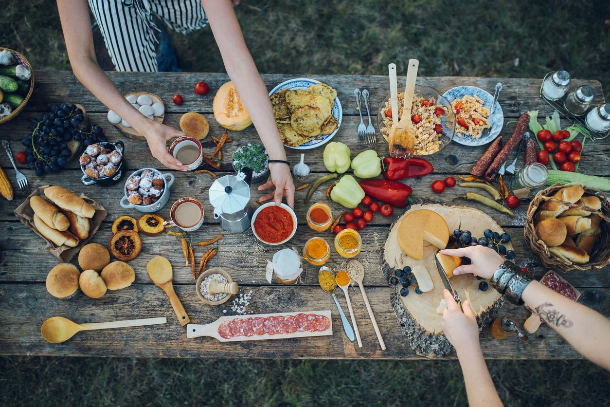 Overhead view of wooden table full of food with people's arms passing food